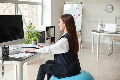 Businesswoman sitting on fitness ball while working in office