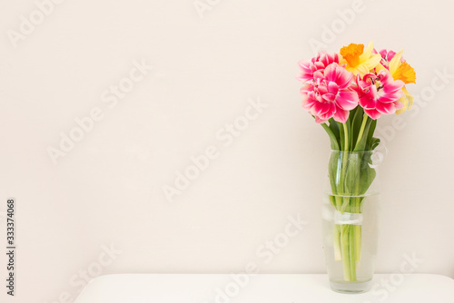 Beautiful spring tulips in vase on table against light background with a copy space