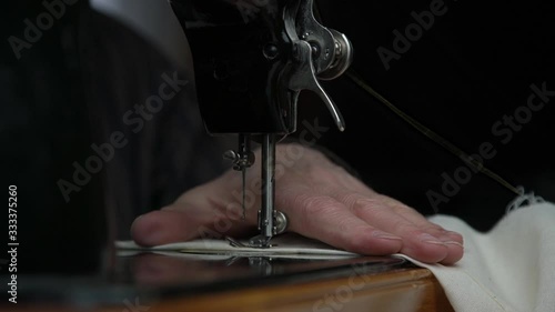 tailor hand rotates hand-wheel and needle rises and goes down making seam on material extreme close view slow motion photo