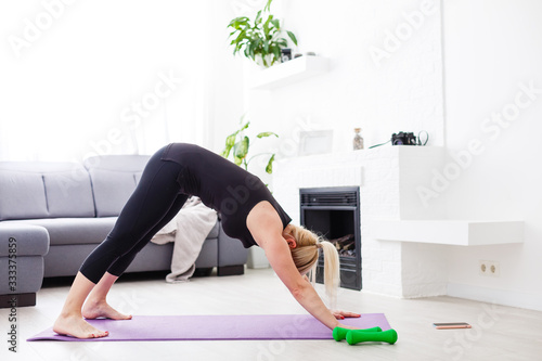 a thin European girl doing stretching exercises at home on a yoga mat, rays of light shine from the window. flare. quarantine sport.