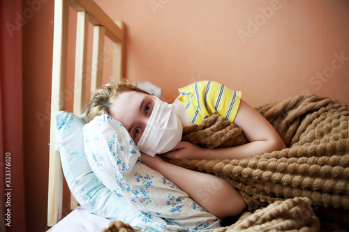  girl in   medical mask under   blanket in bed.