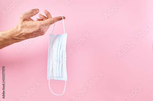 Hand holding medical protective mask on a pink background