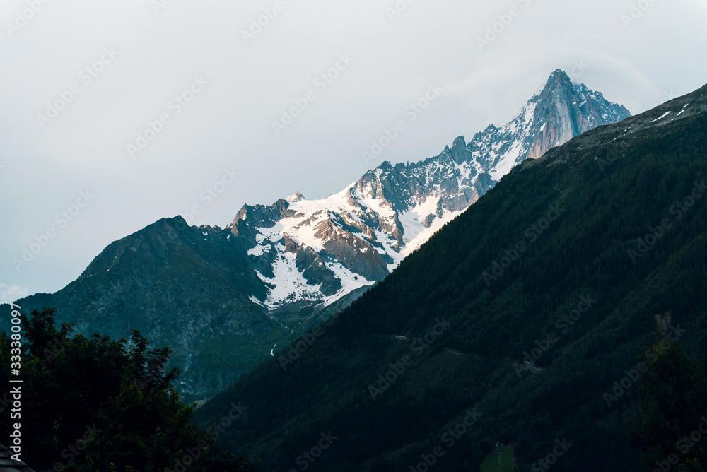 Outdoor landscape in Chamonix. Forest and snow-capped mountains in clouds. Travel and hiking concept