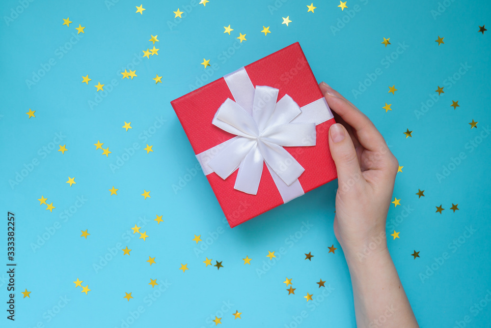 Woman holding red gift box on color blue background with scattered golden stars. Festive greeting card. Holiday concept. Woman holding red gift box on color blue background with scattered golden stars. Festive greeting card. Holiday concept.