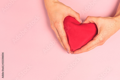  Beautiful young woman s hands holding  plush heart on pastel pink background .