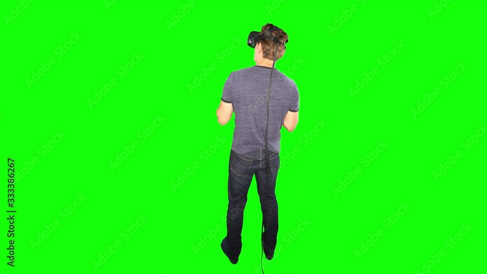 Man looking around in VR from behind. Back of male playing virtual reality on green screen. Reverse shot behind person looking at game world. Enjoying futuristic virtual entertainment at home. Man looking around in VR from behind. Back of male playing virtual reality on green screen. Reverse shot behind person looking at game world. Enjoying futuristic virtual entertainment at home.