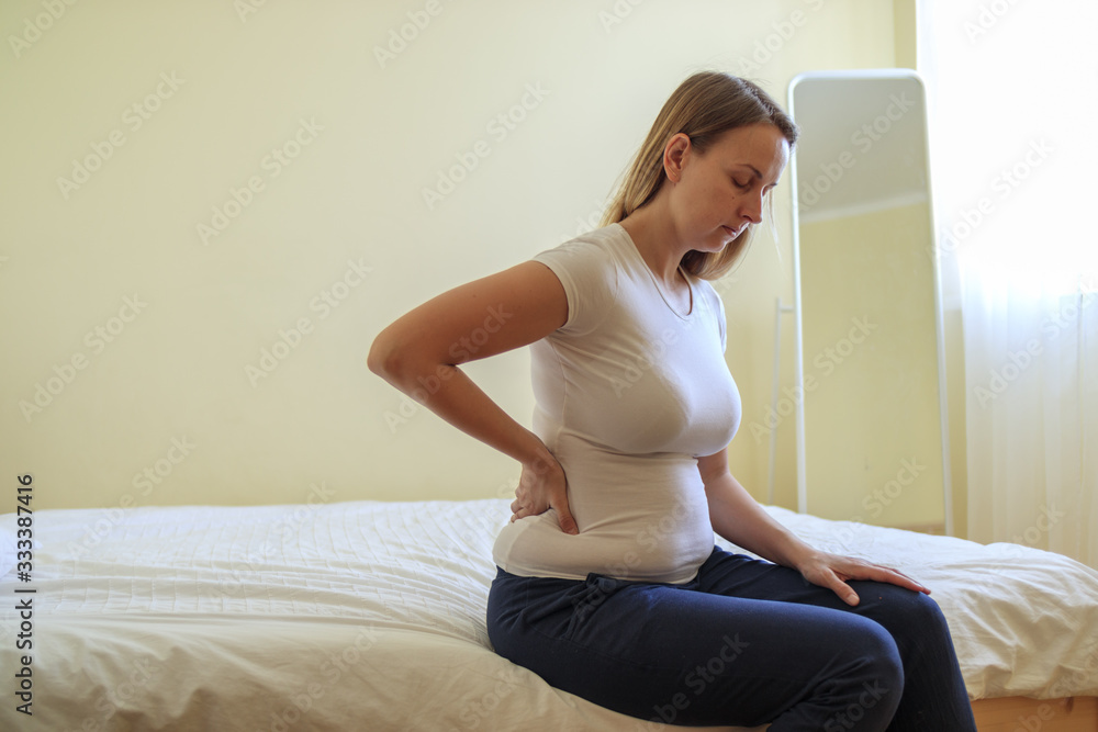 Young plump woman sitting in bedroom with backache Young plump woman sitting in bedroom with backache