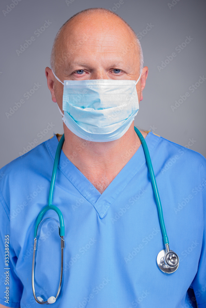 Doctor wearing face mask, blue scrubs and a stethoscope against light background. Doctor wearing face mask, blue scrubs and a stethoscope against light background.
