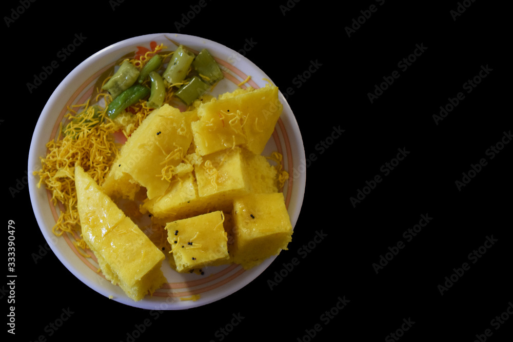 Khaman in plate with sev and mirchi with black background top view Khaman in plate with sev and mirchi with black background top view