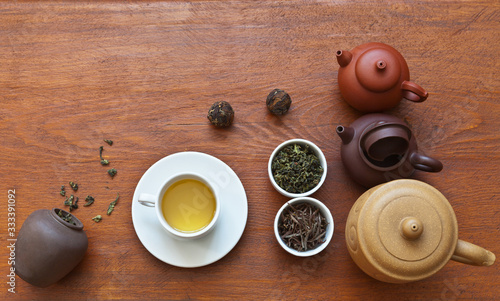 A cup of hot green invigorating tea, traditional ceramic teapots and different types of dry green tea on a wooden background. Green tea is good for diseases, coronovirus infections and colds