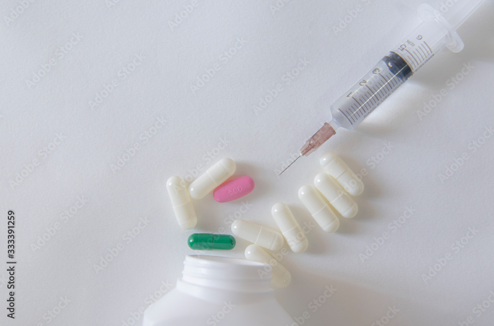 White and green pill capsules on white background near syringe and ...