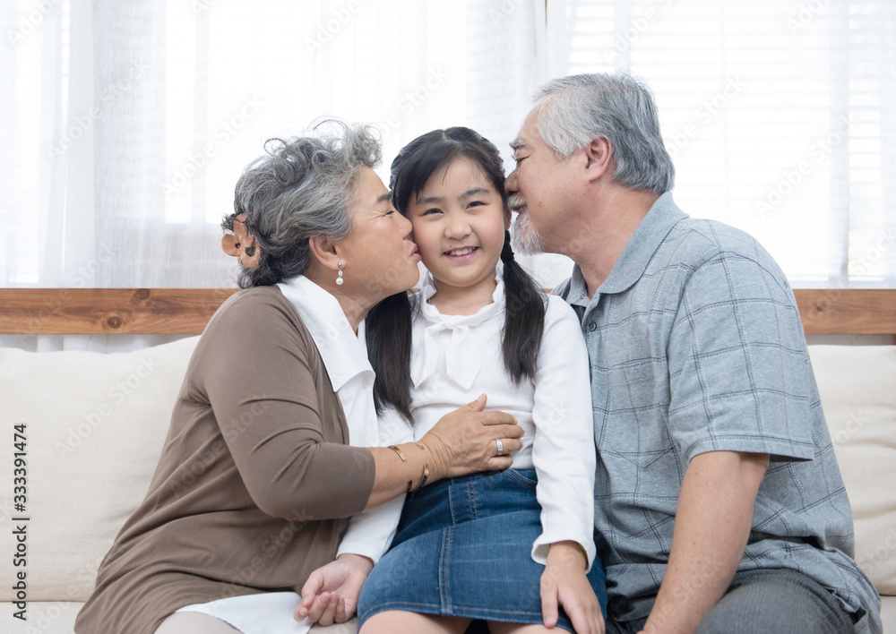 Happy asian grandparents sitting on sofa at home playing and kiss on cheek of little granddaughter Happy asian grandparents sitting on sofa at home playing and kiss on cheek of little granddaughter
