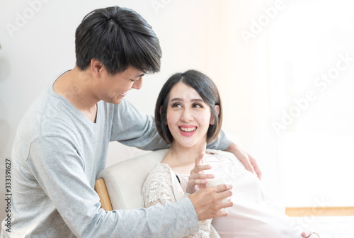 Young happy father prepare milk glass for pregnant mother. Asian Daddy takes care and embrace pregnant woman with love,Space for text.