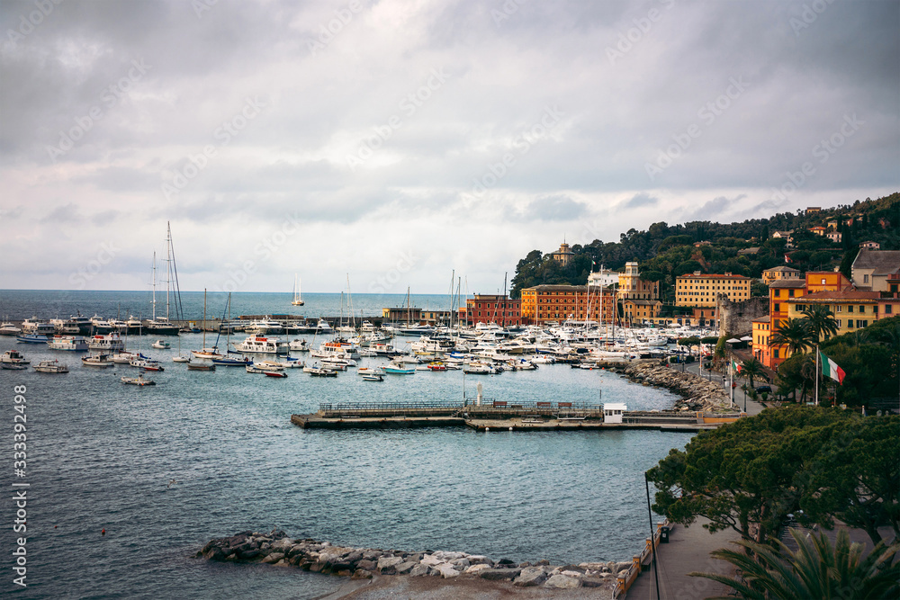 Wide panoramic view of luxury yachts and sailing boats moored in harbor of Santa Margherita Ligure, Italian Riviera. Beautiful mediterranean landscape with cloudy blue sky.