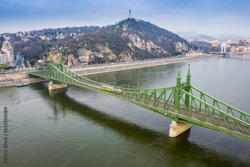 Budapest, Hungary - Aerial view of Liberty Bridge (Szabadsag hid) on a Spring morning with yellow trams and Statue of Liberty at background. Empty bridge and roads due to Coronavirus quarantine