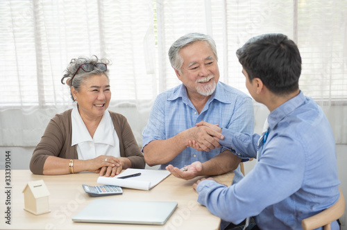 Smiling satisfied senior couple making sale purchase deal concluding contract hand get house key from real estate agent,happy older family and broker shake hands agreeing to buy new house at meeting.