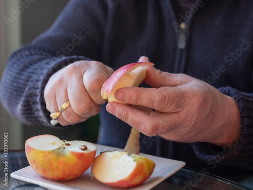 Old man hands peeling organic red Pink Lady apple outside over a bowl of apple slices