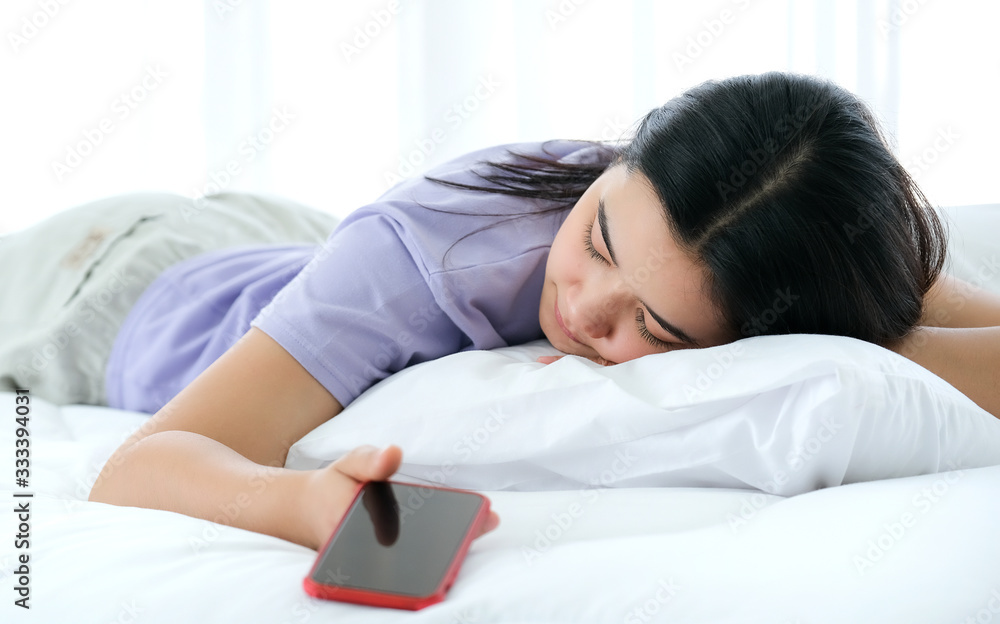 Beautiful Asia woman lying on the bed and holding smartphone in her hand. sleep in the white bedroom, focused on women. Feeling tried. Social addicted, modern life style and relaxation concept. Beautiful Asia woman lying on the bed and holding smartphone in her hand. sleep in the white bedroom, focused on women. Feeling tried. Social addicted, modern life style and relaxation concept.