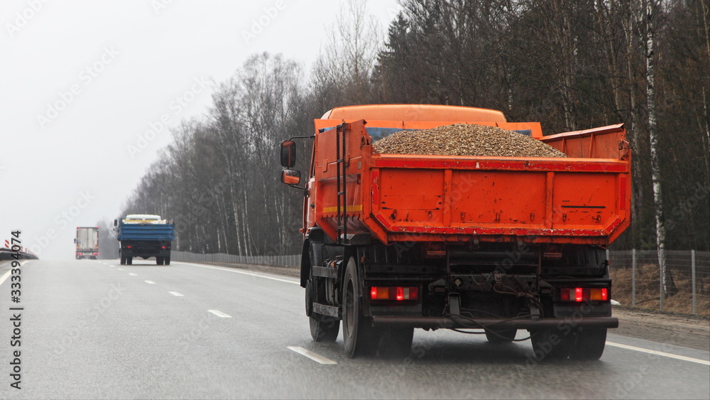 Orange loaded dump truck with gravel drive on highway road at spring day
