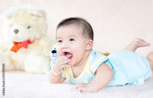 Closeup asian baby infant laying comfortably on bed playing with bear doll on softness cushion,Baby development concept.
