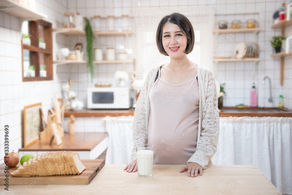 Portrait beautiful young asian pregnant woman drink milk glass standing in kitchen at home.Health care and love of pregnancy mother’s day concept. Portrait beautiful young asian pregnant woman drink milk glass standing in kitchen at home.Health care and love of pregnancy mother’s day concept.