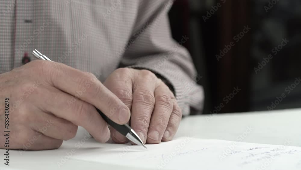 elderly man puts fast signature on paper sheet with lovely private letter sitting at white table extreme close view elderly man puts fast signature on paper sheet with lovely private letter sitting at white table extreme close view