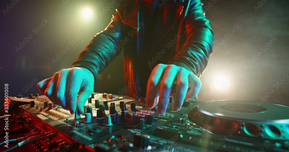 A cool bearded dj standing at the mixer controller, composing a new mix and rocking the party in a nightclub - nightlife concept 4k footage