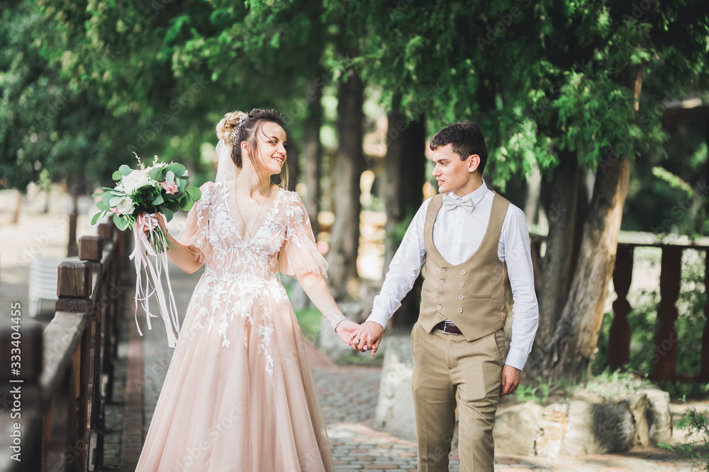 Stylish couple of happy newlyweds walking in the park on their wedding day with bouquet Stylish couple of happy newlyweds walking in the park on their wedding day with bouquet