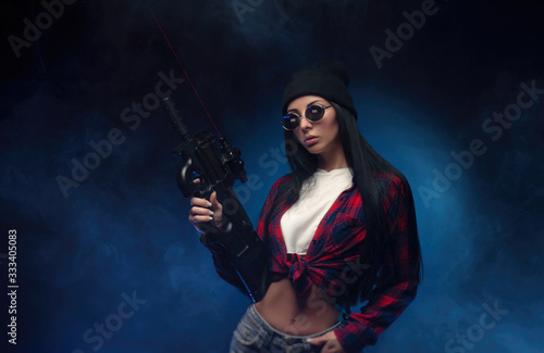 a girl in a checked shirt on a dark background with an automatic rifle