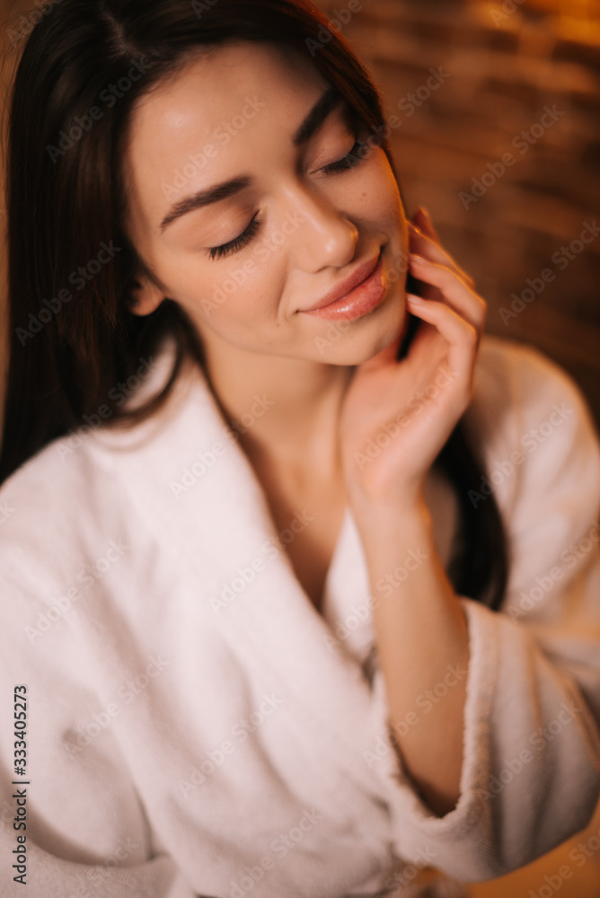 Close-up portrait of face of beautiful young female in white bathrobe with closed eyes on background of brick wall. Concept of luxury professional massage. Close-up portrait of face of beautiful young female in white bathrobe with closed eyes on background of brick wall. Concept of luxury professional massage.