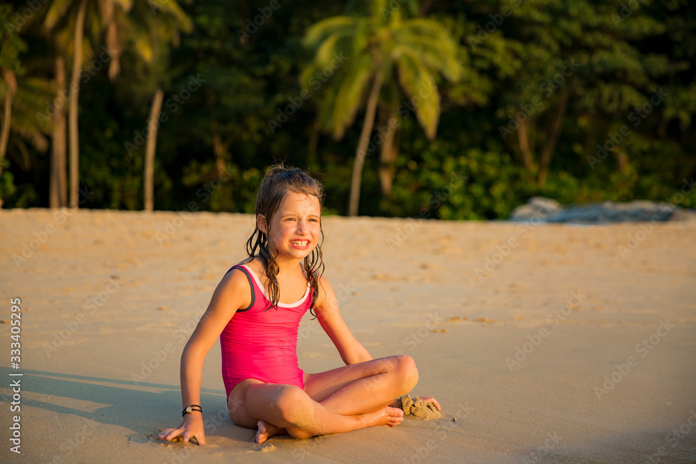 Cute happy little girl playing with sand on the beach in swimming suit ...