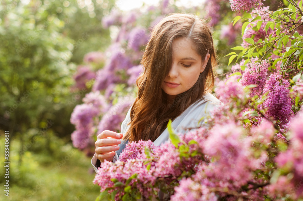 Young pretty girl in closed eyes enjoys the smell of lilac in the early morning in the garden.. Young pretty girl in closed eyes enjoys the smell of lilac in the early morning in the garden..