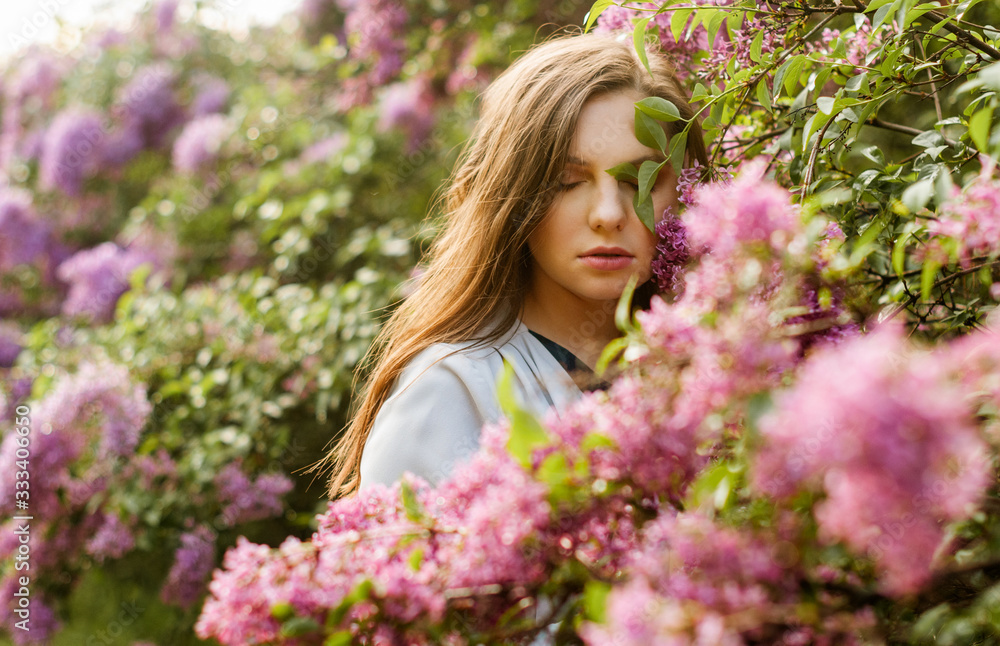 Young pretty girl in closed eyes enjoys the smell of lilac in the early morning in the garden.. Young pretty girl in closed eyes enjoys the smell of lilac in the early morning in the garden..