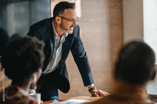 close up of businessman standing over boardroom table in front of South African coworkers during a diverse corporate meeting photo