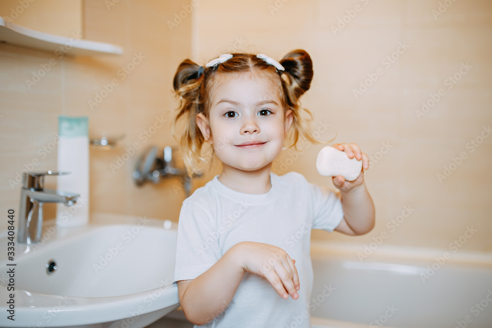 A child shows soap in bathroom. A kid is washing hands with anti-infective soap. Baby girl washing hands and holding white soap.