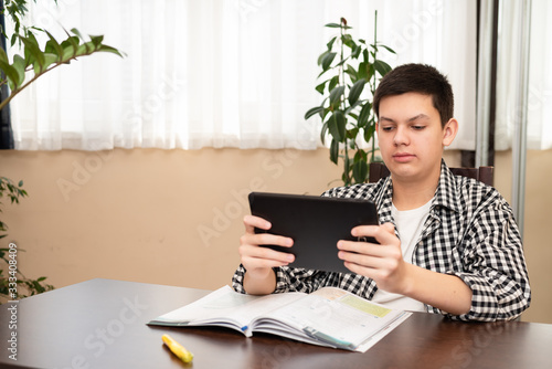 Obraz na płótnie Caucasian teen boy learning language online using digital tablet looking at screen, doing school tasks at home, writing notes, listening lecture. E-learning and distance education concept. w salonie