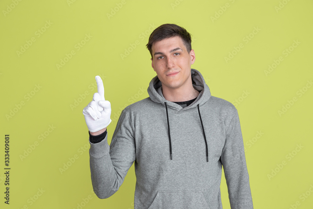 Pointing up. Caucasian man's portrait isolated on yellow studio background. Freaky male model using gloves. Concept of human emotions, facial expression, sales, ad. Unusual appearance. Pointing up. Caucasian man's portrait isolated on yellow studio background. Freaky male model using gloves. Concept of human emotions, facial expression, sales, ad. Unusual appearance.