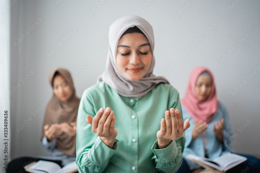 three veiled women sit on the floor praying while learning to read the holy book of the Al-Qoran together in the house three veiled women sit on the floor praying while learning to read the holy book of the Al-Qoran together in the house