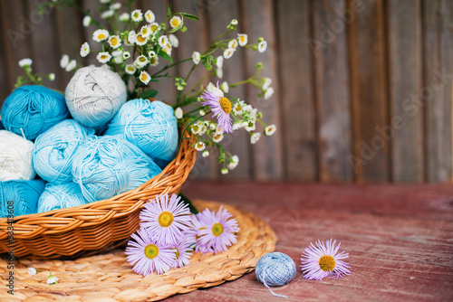 Women s hobby. Crochet and knitting. Working space. Blue yarn in basket  flowers  knitting needles  scissors on the wooden background in the cozy home in rustik style.