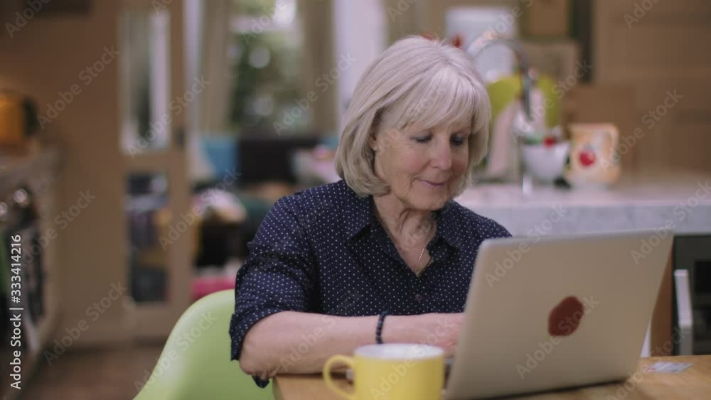Senior woman buying online using laptop on kitchen table Senior woman buying online using laptop on kitchen table