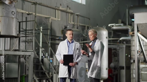 Wallpaper Mural Three quarter length medium shot of two quality control experts in white coats, middle aged female and male, talking standing in factory. Man listening to female colleague Torontodigital.ca