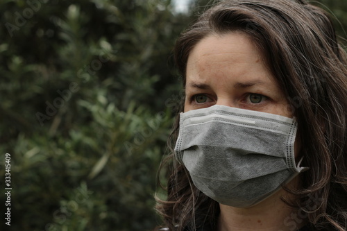 Young Australian woman wearing a paper surgical protective face mask to guard against catching or spreading infectious diseases and viruses in a public park, Victoria, Australia