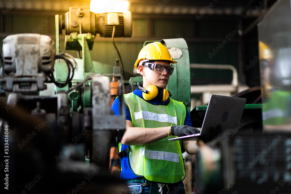 Portrait Engineer man working with computer laptop or tablet at factory Equipment. Chief Engineer in the Hard Hat Holds Laptop at the industrial facility. Portrait Engineer man working with computer laptop or tablet at factory Equipment. Chief Engineer in the Hard Hat Holds Laptop at the industrial facility.