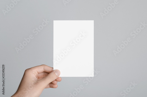 A6 Flyer / Postcard / Invitation Mock-Up - Male hands holding a blank flyer on a gray background.