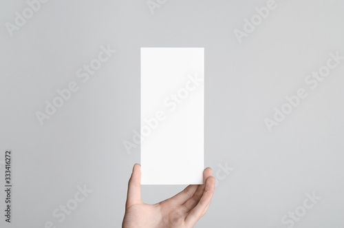 DL Flyer Mock-Up - Male hands holding a blank flyer on a gray background.
