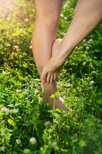 beautiful female legs with an elegant pedicure dance barefoot on the lush green grass and flowers in the sunset in spring or summer