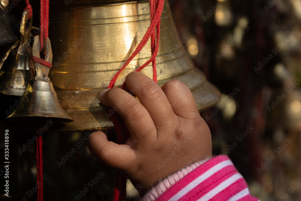A BABY CHILD GIRL HAND TOUCHES A BIG BRASS BELL IN TILINGA MANDIR