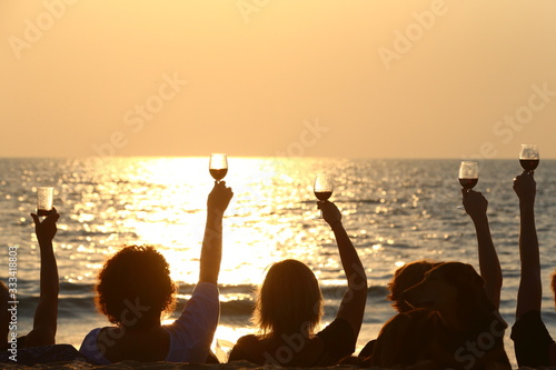 silhouette of a group of friends holding up their glasses of wine while enjoying a sunset together
