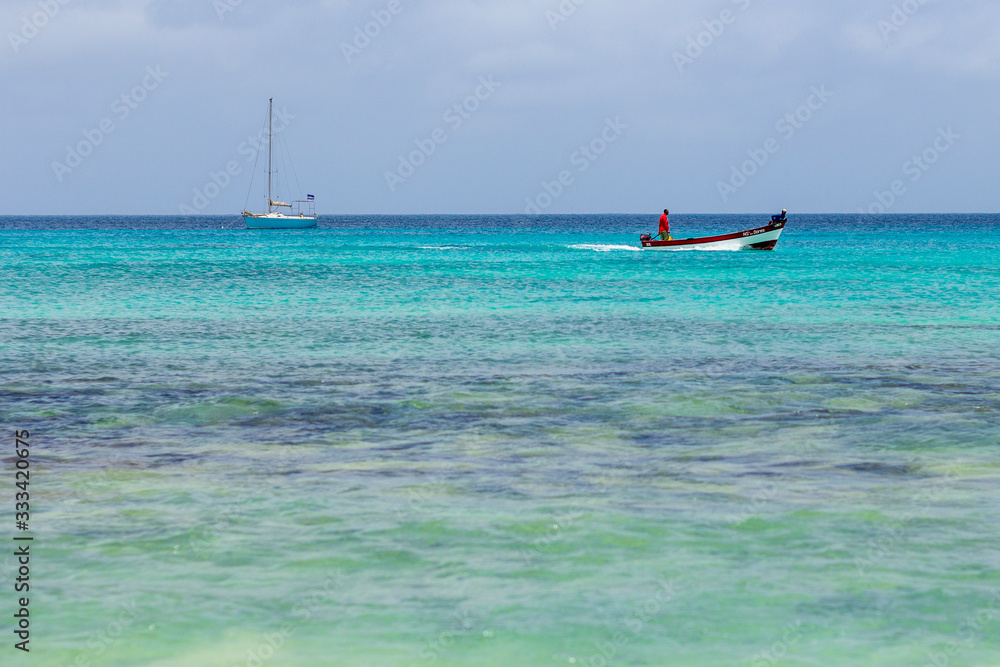 Fisherman in boat with yacht on turquoise blue sea in Santa Maria, Cape Verde