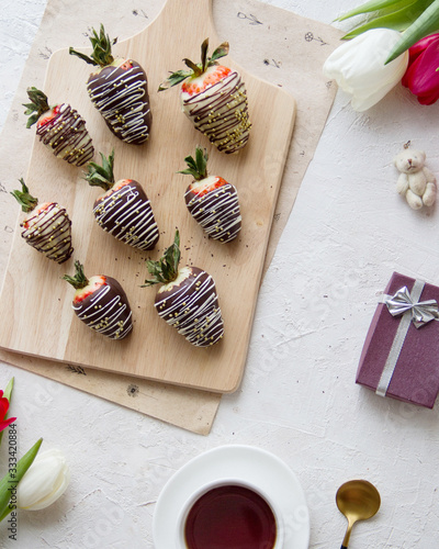 Chocolate-covered strawberries, coffee and flowers on the table. Light photo, top view.